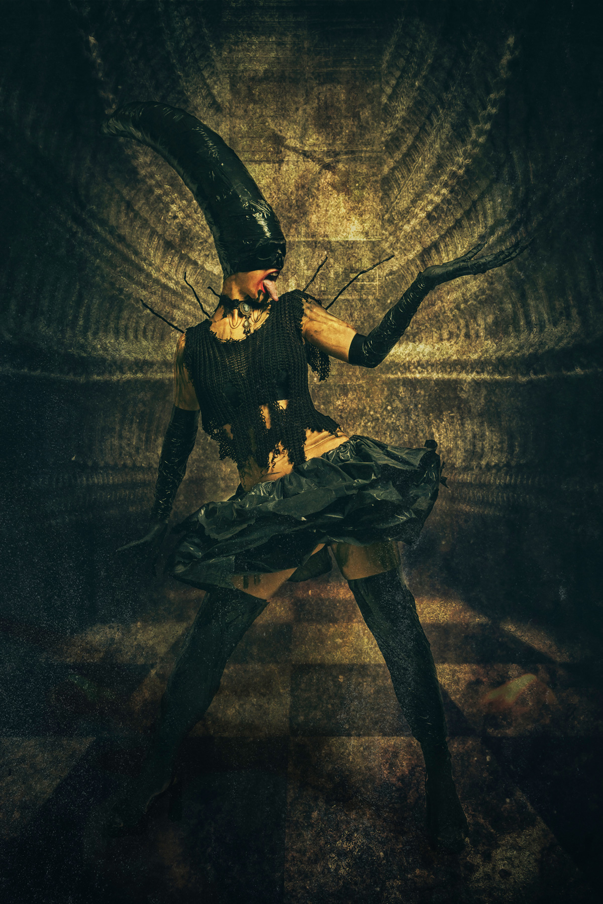 A full-body fine art portrait of a dark, avant-garde figure wearing a tall, curved black headpiece, tattered black clothing, and long gloves, posing dynamically in a gritty, industrial setting with a checkered floor.